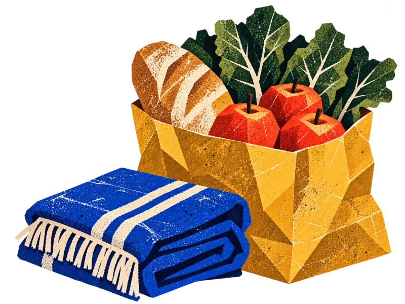 A paper bag of bread, greens and red apples beside a folded blue blanket.